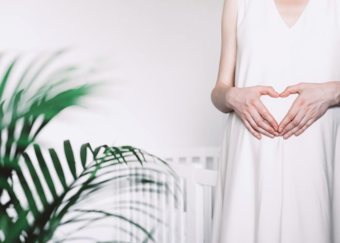 Pregnant woman in white dress making heart on pregnant belly.